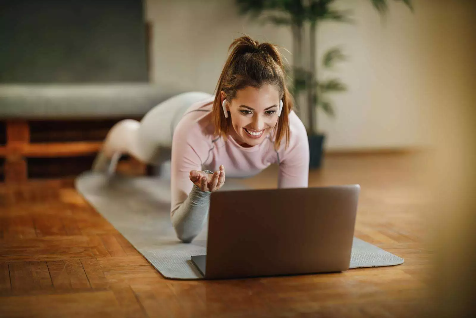 An attractive young woman using laptop to record her vlog about healthy living while doing plank exercises at home.