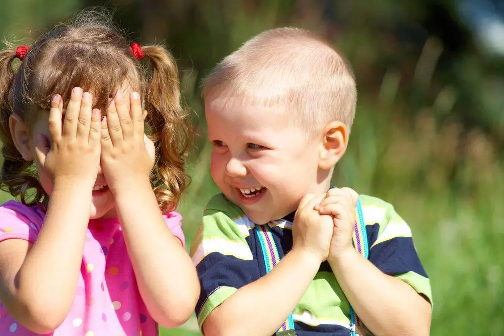 Two funny kids are playing, covering his face with his hands.