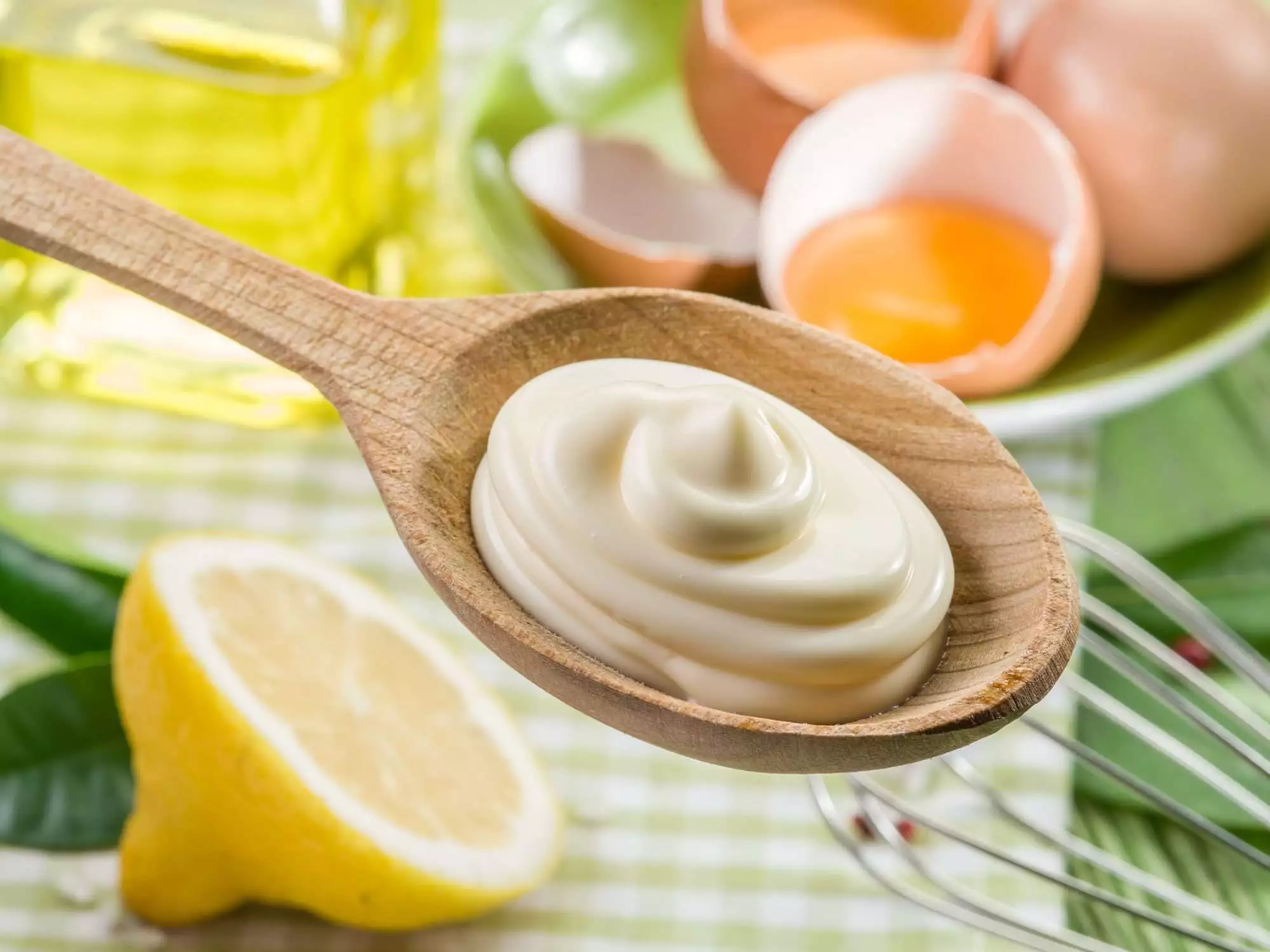 Natural mayonnaise sauce in the wooden spoon and its ingredient on the background.