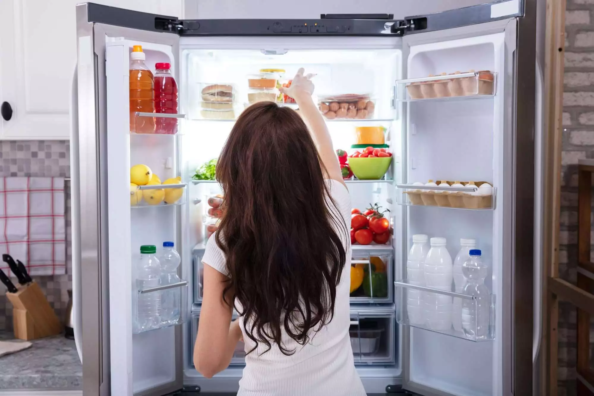 Rear View Of A Young Woman Taking Food To Eat From Refrigerator